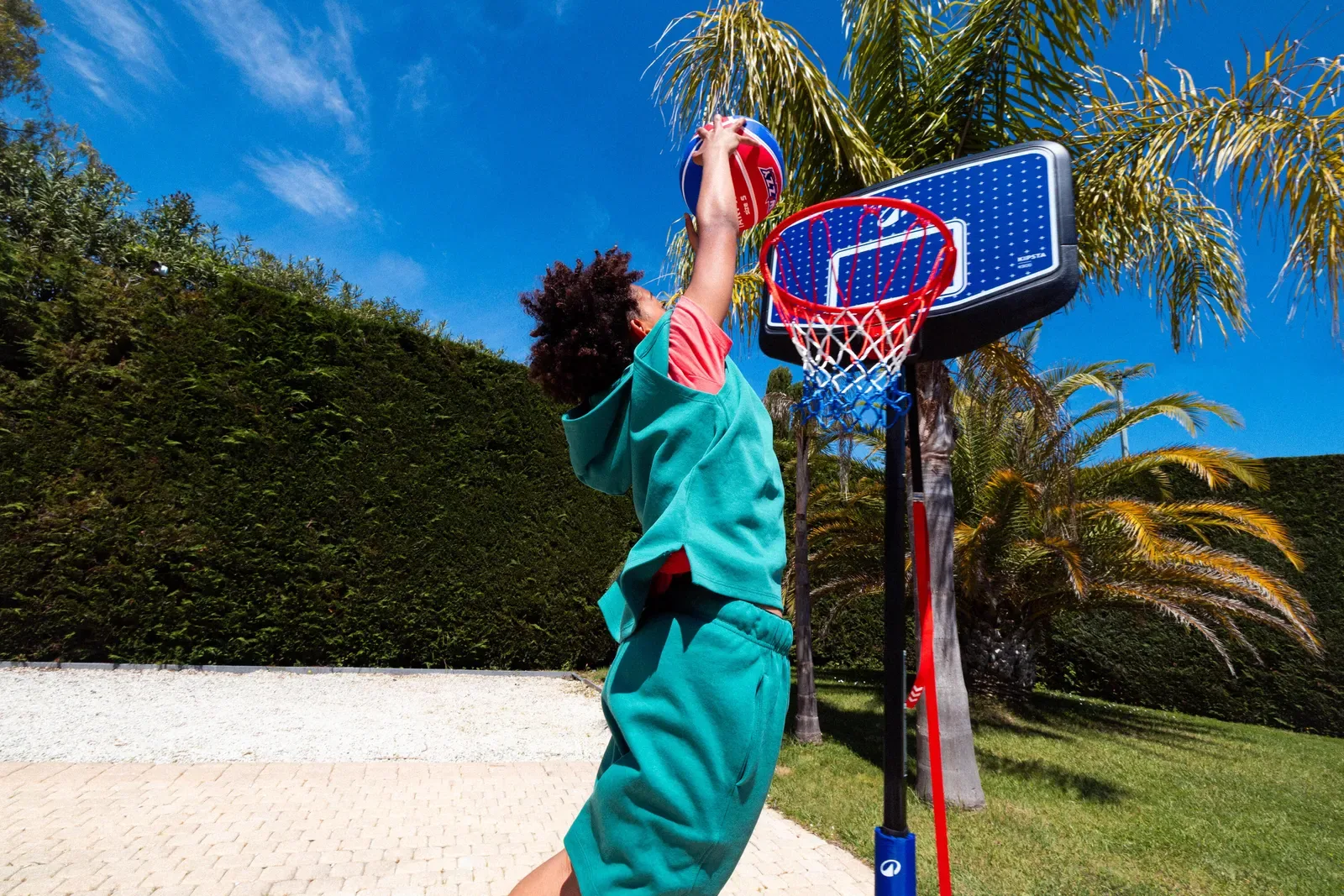 Teenager dunking a basketball on a portable hoop in a backyard