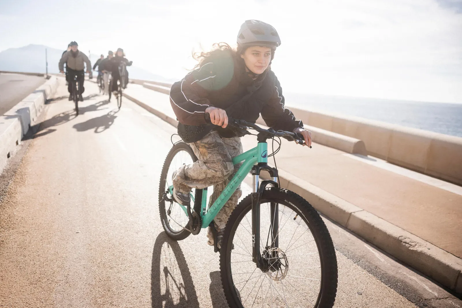 Teenager in a helmet riding a mountain bike along a seaside path with friends behind