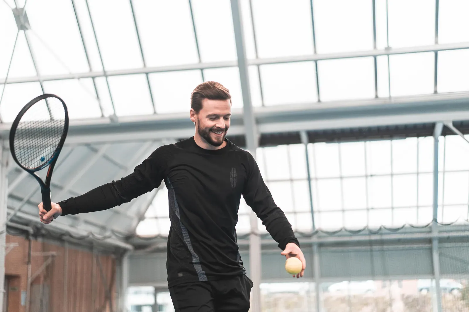 Smiling tennis player with racket and ball on an indoor court