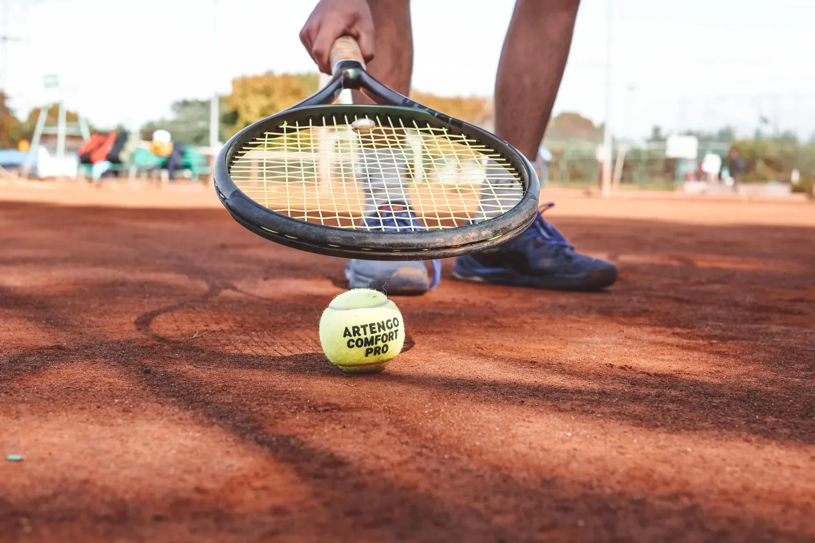 Player scooping a tennis ball up with a racket on a clay court