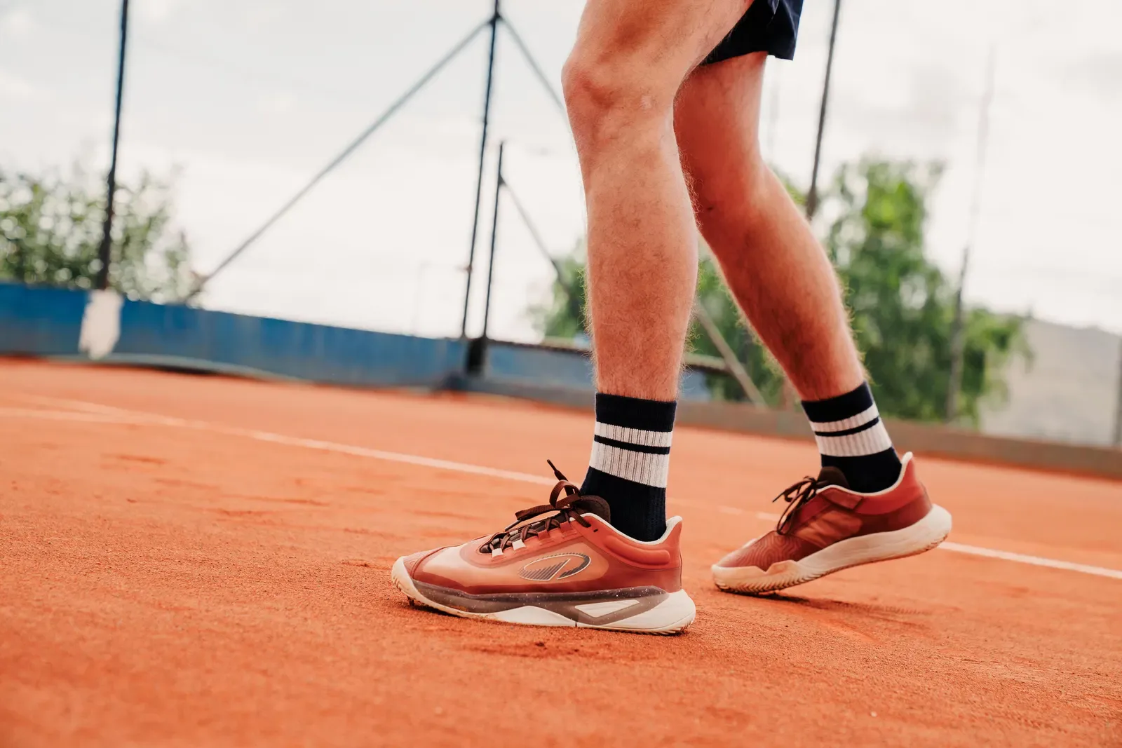 Player walking along the baseline of a clay tennis court in court shoes