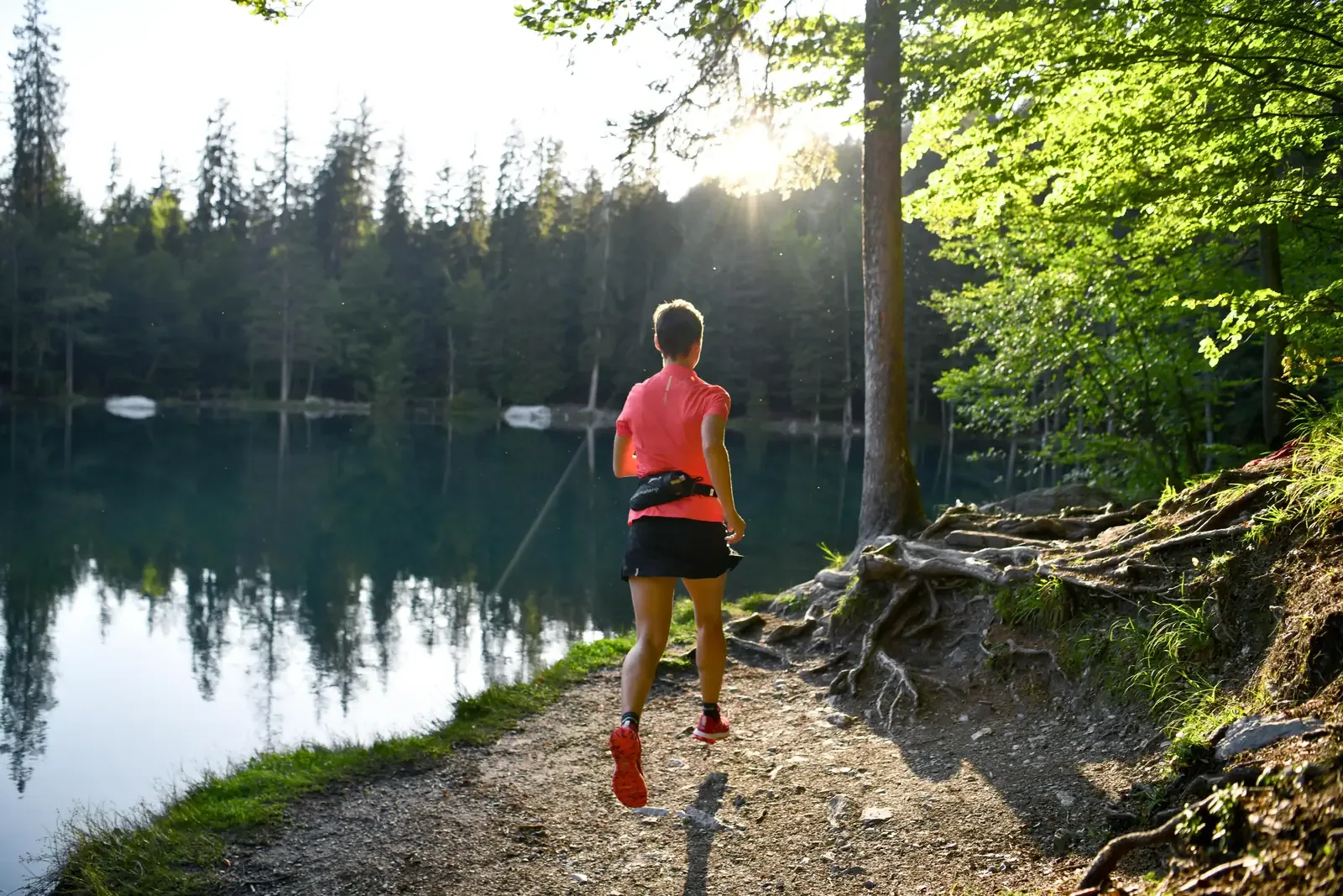 Trail runner on a dirt path along a forest lake in soft morning light