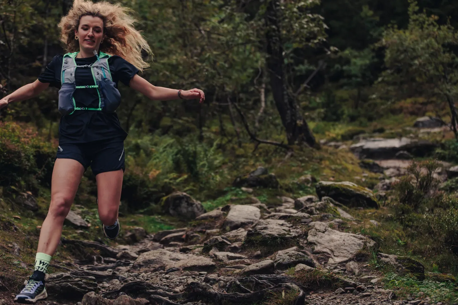 Woman moving quickly down a rocky path through green forest