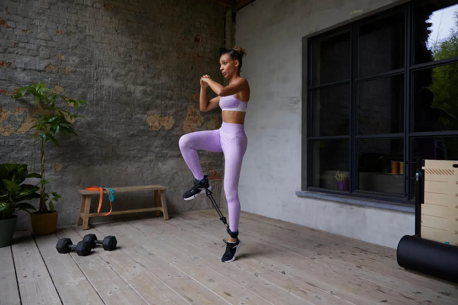 Woman doing a knee drive with a resistance band at home, dumbbells on the floor