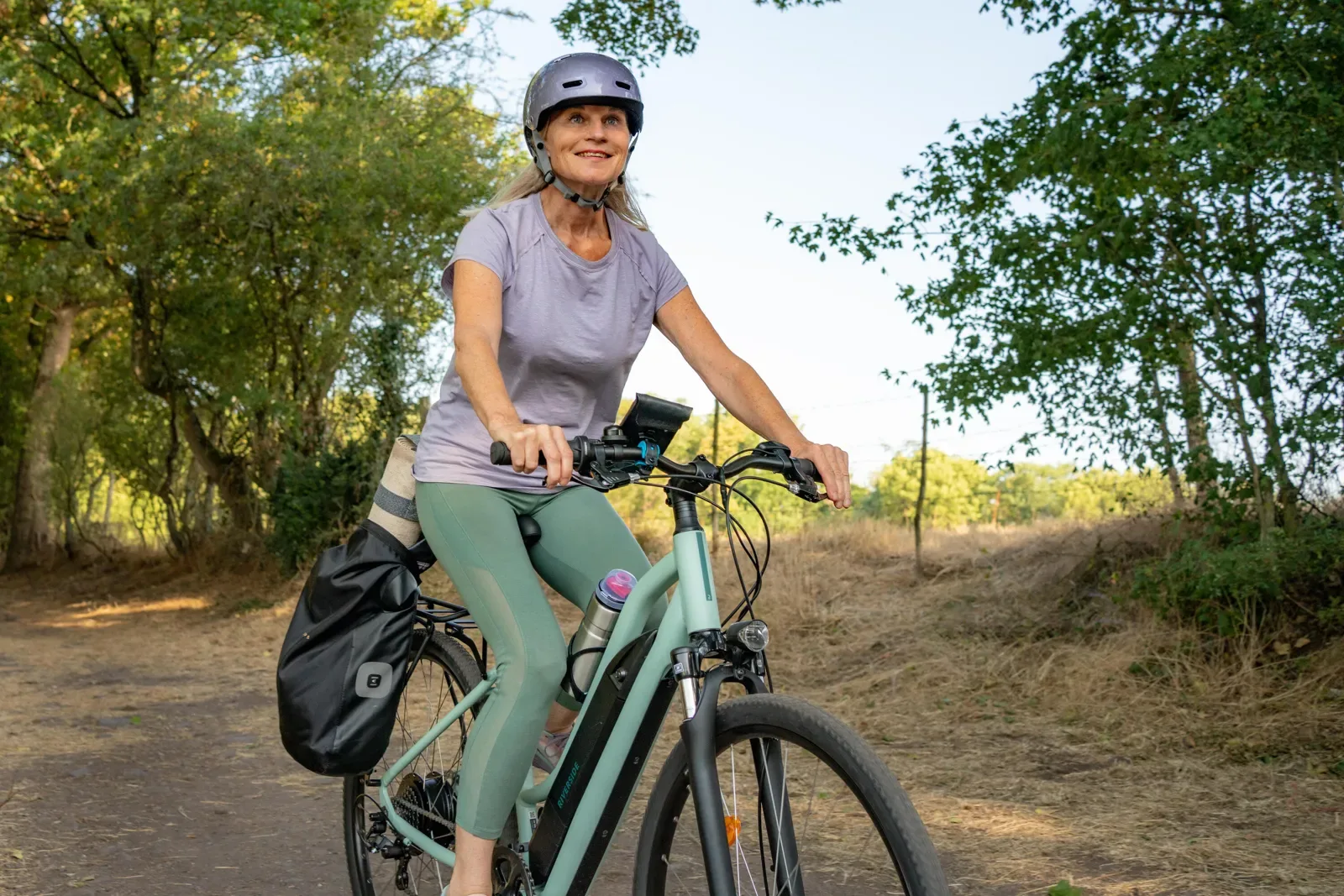 Woman riding an e-bike with a rear pannier on a dirt path