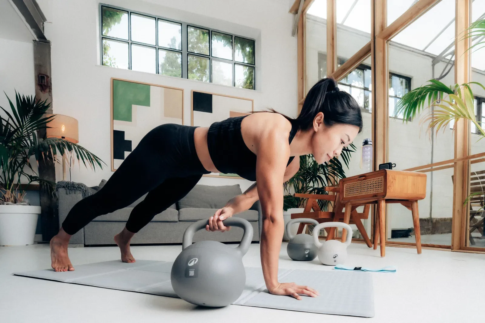 Woman holding a plank with one hand on a kettlebell on a mat in her living room