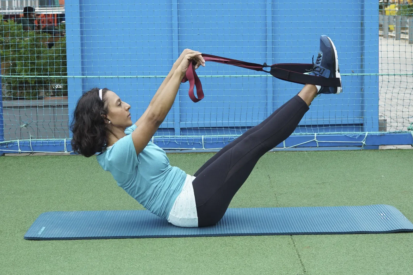 Woman holding a V-sit on an exercise mat, using a strap around her feet